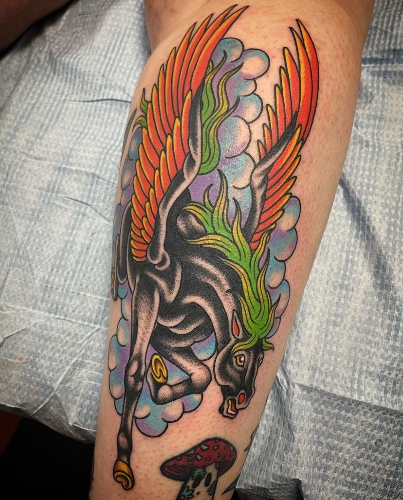Colorful tattoo of a snarling black creature with orange wings on a person’s calf