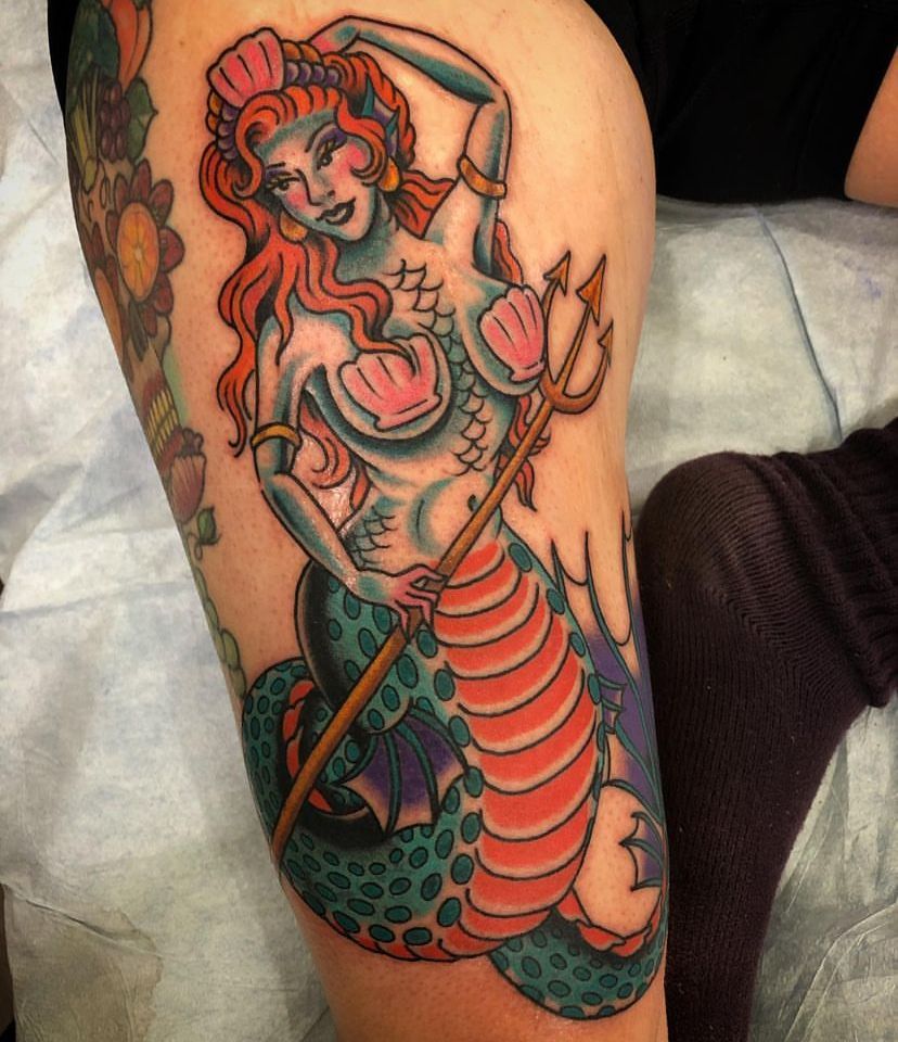 Colorful mermaid tattoo with red hair, teal scales, and a pink flower on a leg