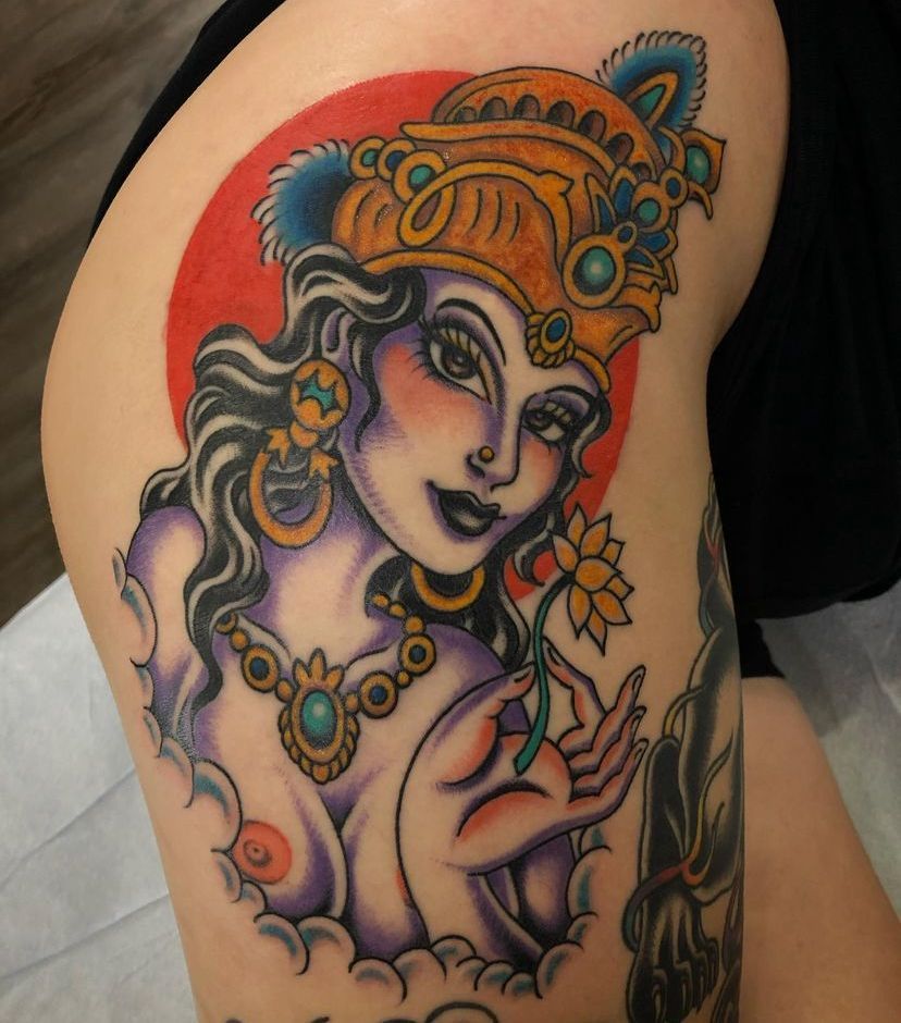 Colorful tattoo of a jeweled, crowned woman with flowing hair and flowers on an upper arm
