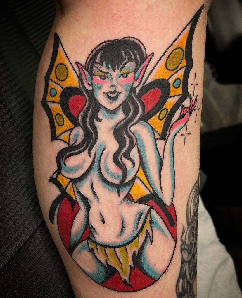 Colorful fairy tattoo with black hair, red-and-yellow wings, and a playful expression on skin.