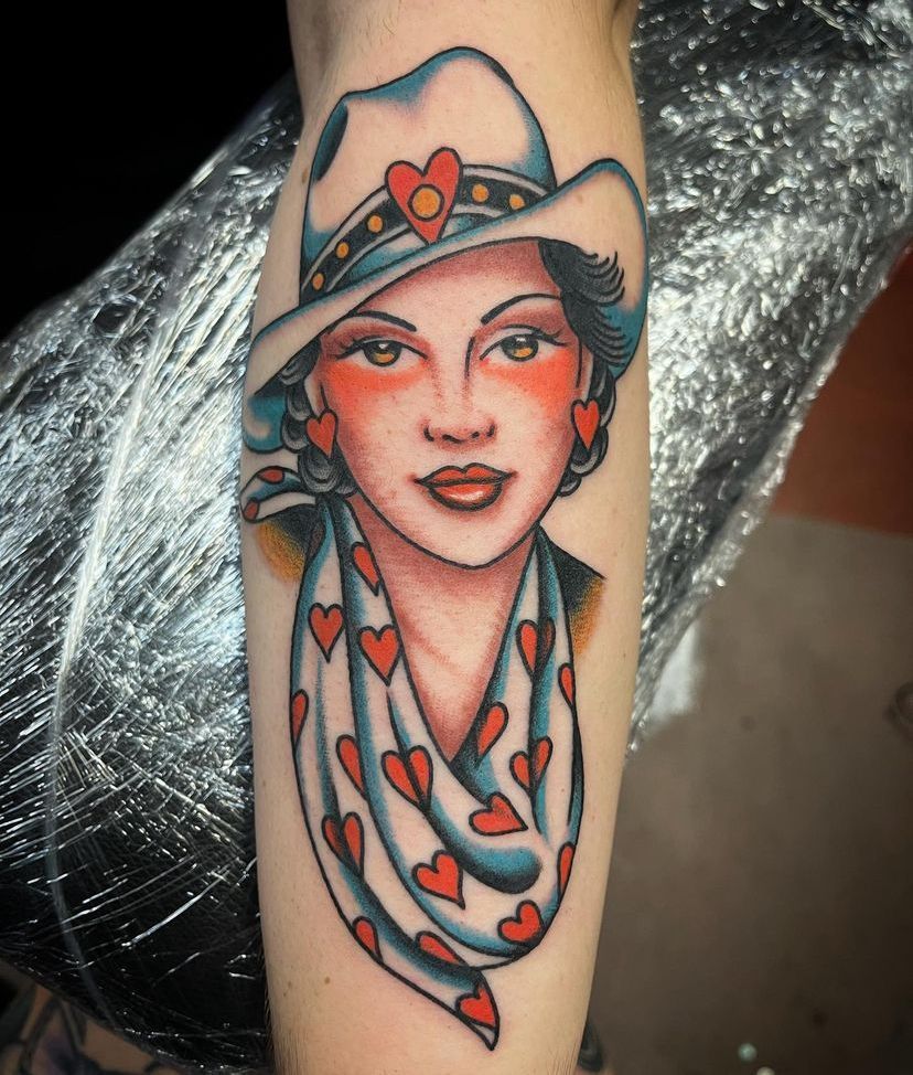 Colorful tattoo of a stylized woman’s face with a heart-decorated headscarf and scarf on an arm