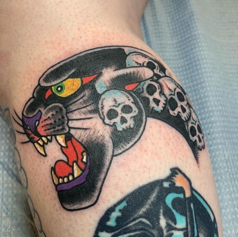 Panther tattoo with skull pattern and open mouth on skin, in black, gray, red, and yellow