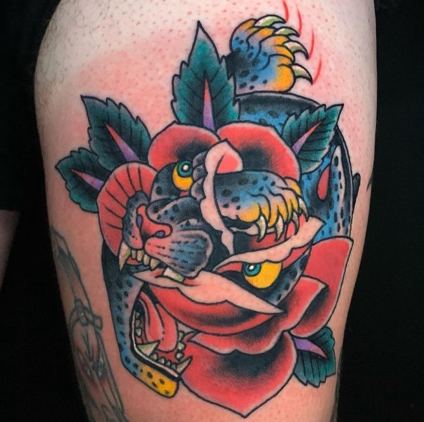 Colorful tattoo of a snarling panther and red rose with teal leaves on skin