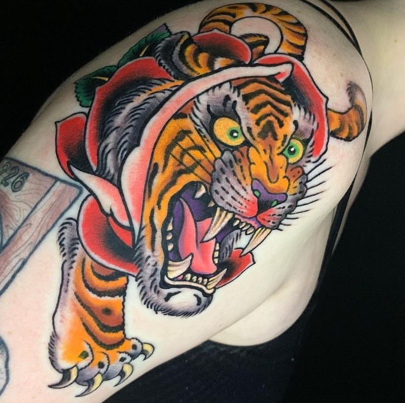 Colorful tiger tattoo on a person’s upper arm, with orange, black, red, and green details.