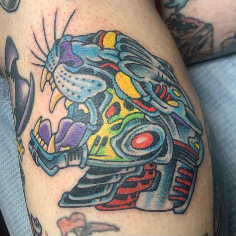 Colorful tattoo of a stylized mechanical cat head with purple, blue, red, and yellow details on skin