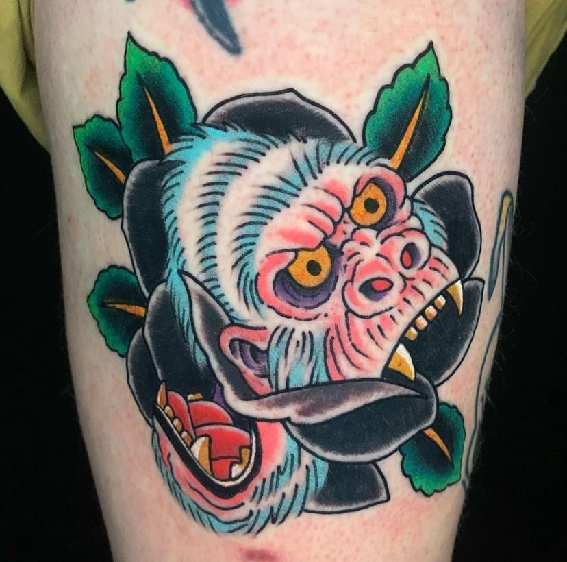 Colorful tattoo of a snarling, stylized monkey face with green leaves on a person's leg