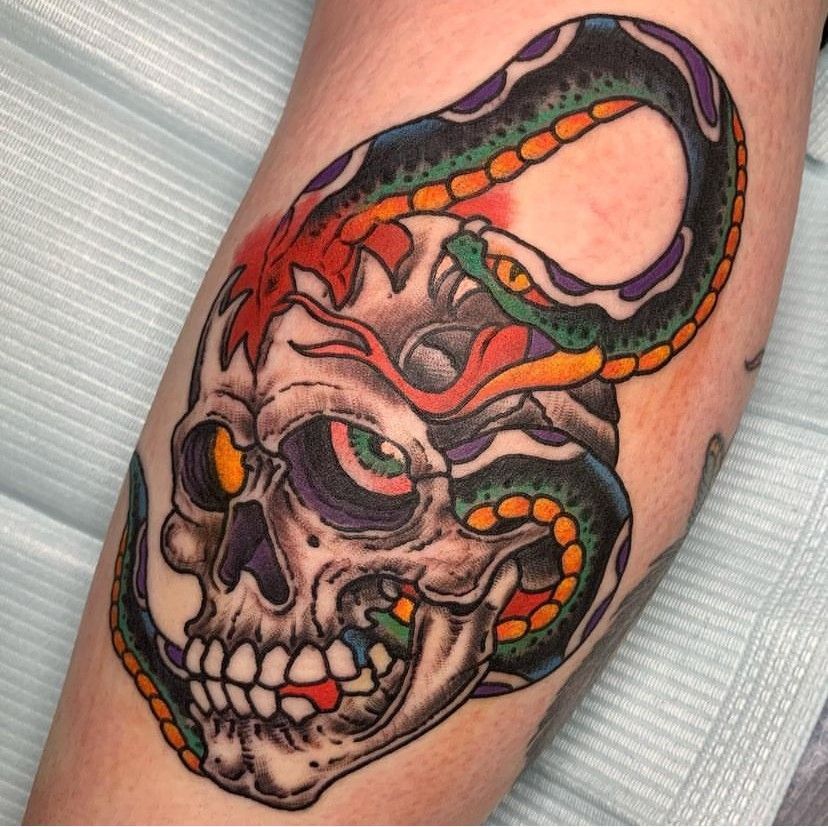 Colorful tattoo of a skull wrapped by a green and red snake on a forearm