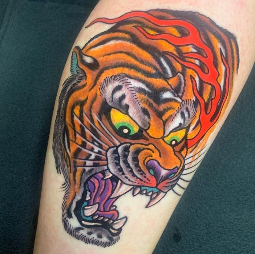 Colorful roaring tiger tattoo on a person’s arm, with orange, black, and purple details.