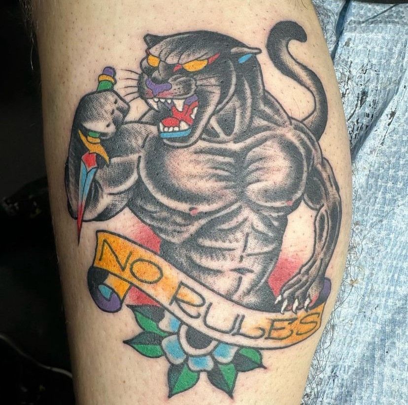 Tattoo of a snarling black panther with a dagger and banner reading “NO RULES” on skin