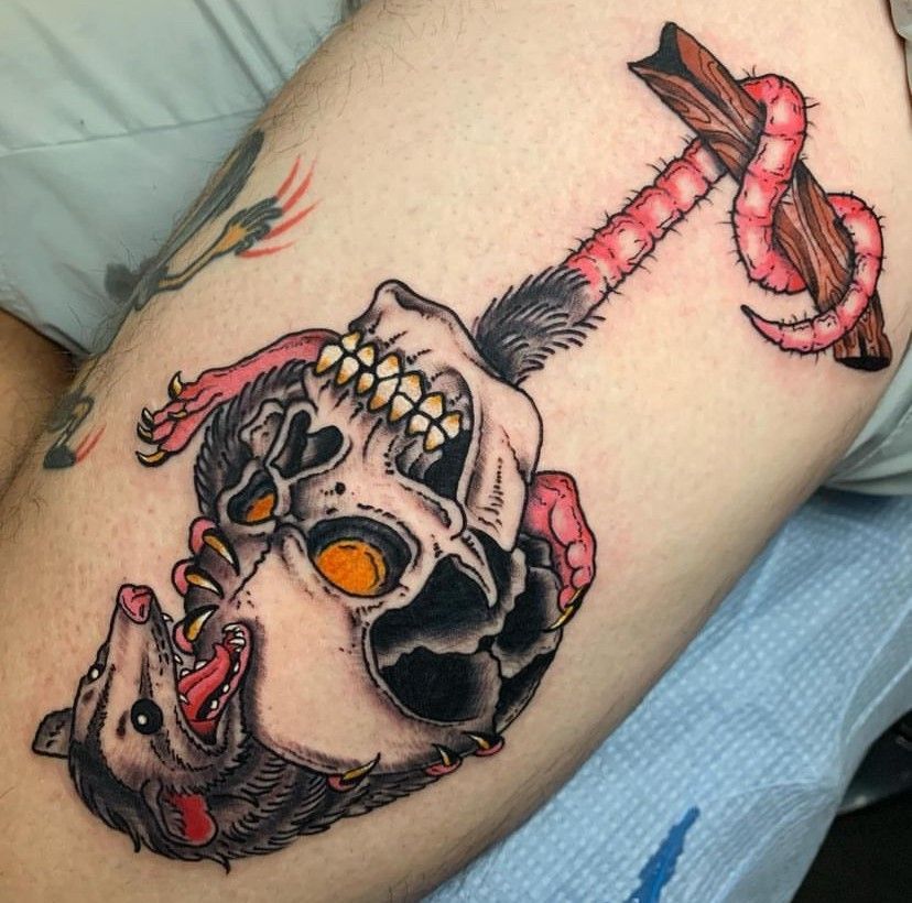 Tattoo of a skull with orange eyes and a pink-wrapped sword on skin