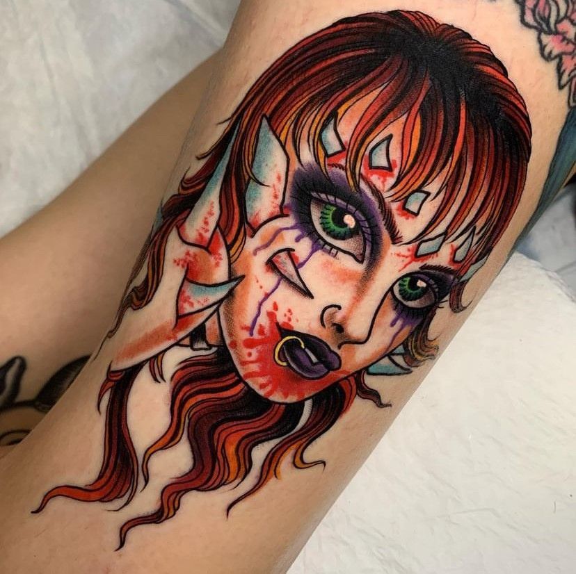 Tattoo of a stylized face with red hair, green eyes, and bold black-and-red shading on an arm