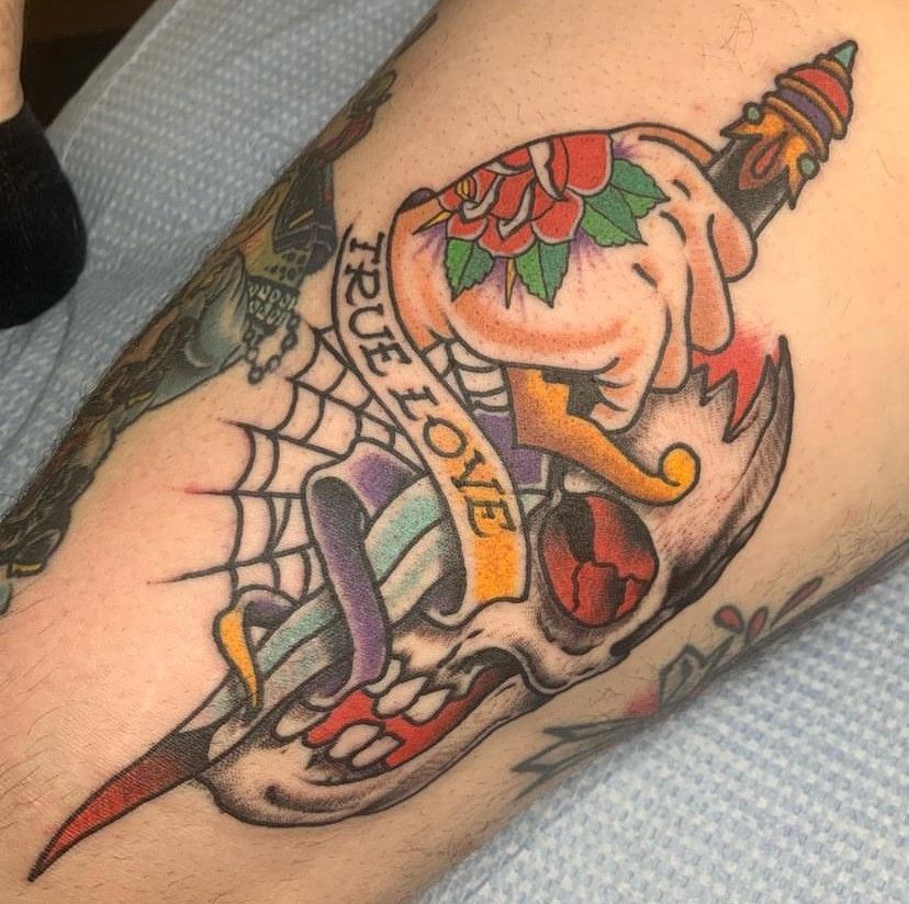 Colorful skull tattoo with roses, web, and banner reading “TRUE LOVE” on a forearm