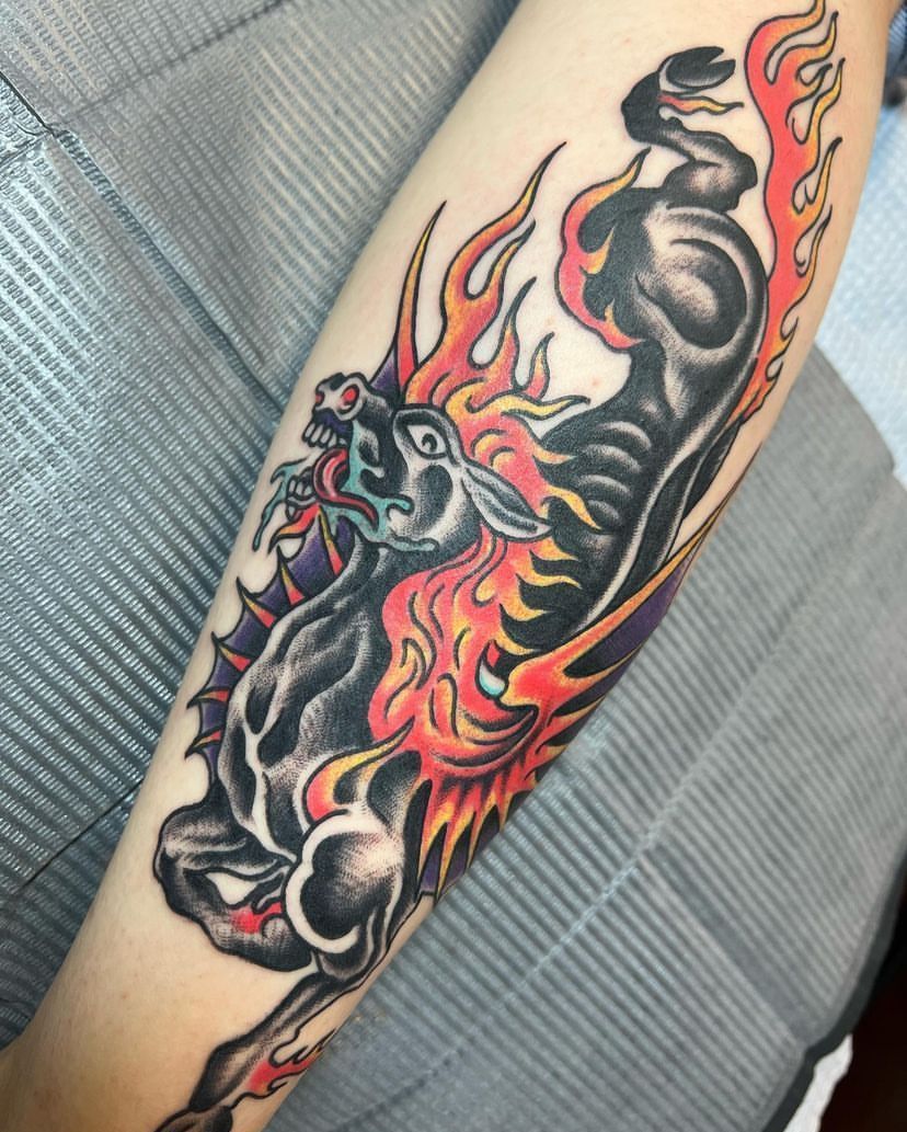 Colorful dragon tattoo on a forearm, with flames in black, red, orange, and gray.