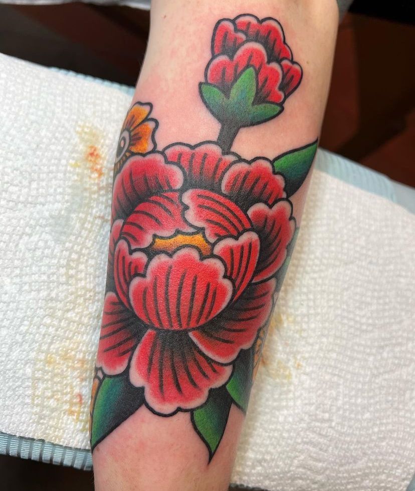 Close-up of a forearm with a colorful red-and-green floral tattoo.