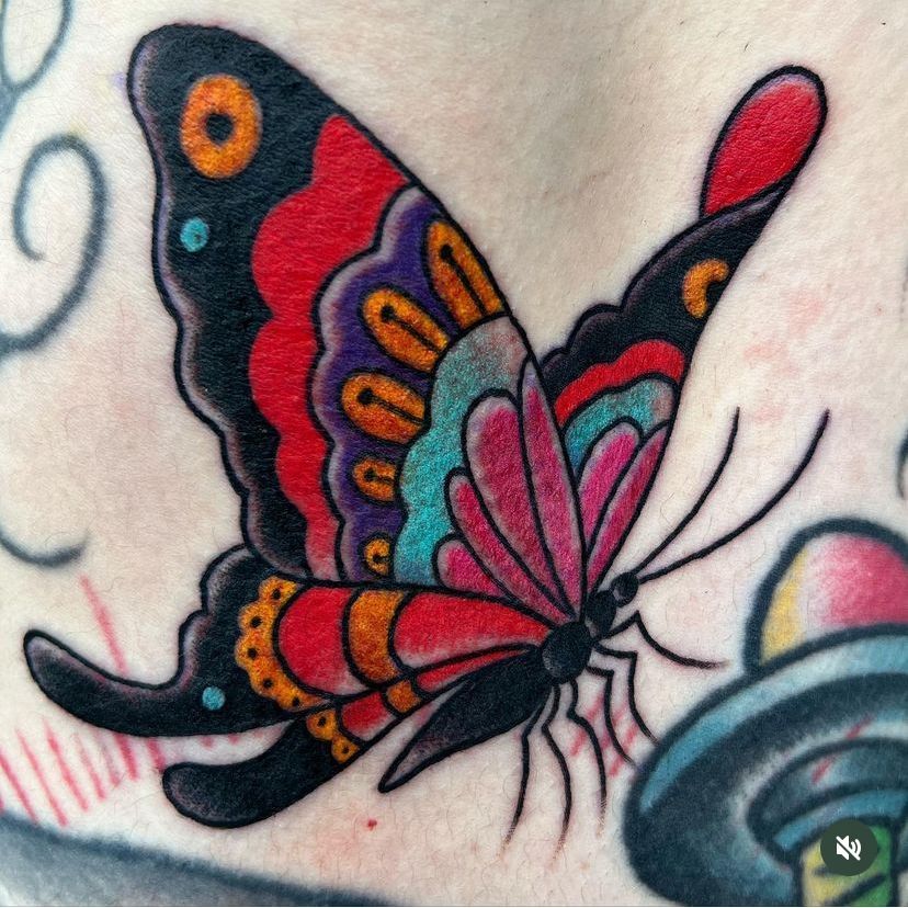 Colorful butterfly tattoo with black, pink, red, and orange wings on skin