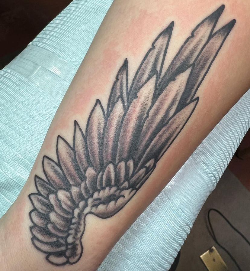 Black-and-gray feathered wing tattoo on an ankle or lower leg