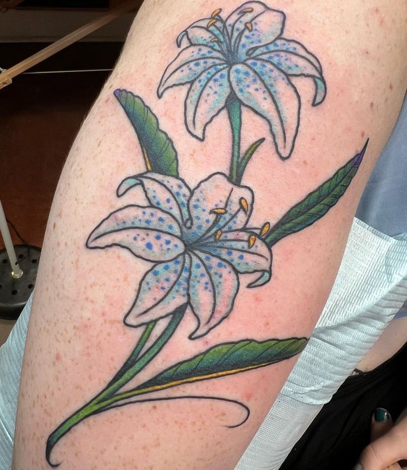 Blue lily tattoo on an arm with green leaves and outlined petals