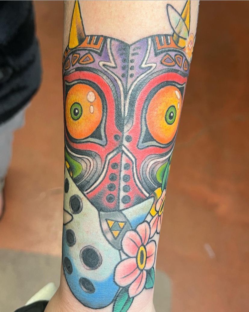 Colorful owl tattoo on a forearm with orange eyes, teal accents, and a pink flower near the wrist