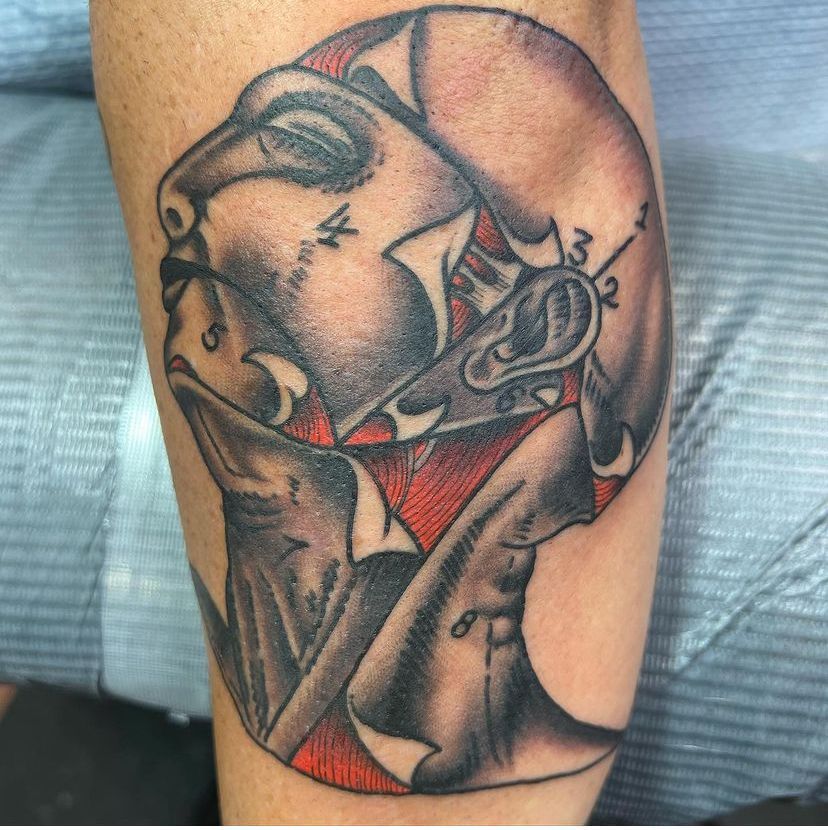 Tattoo of a grayscale abstract face with red accents on a person’s arm