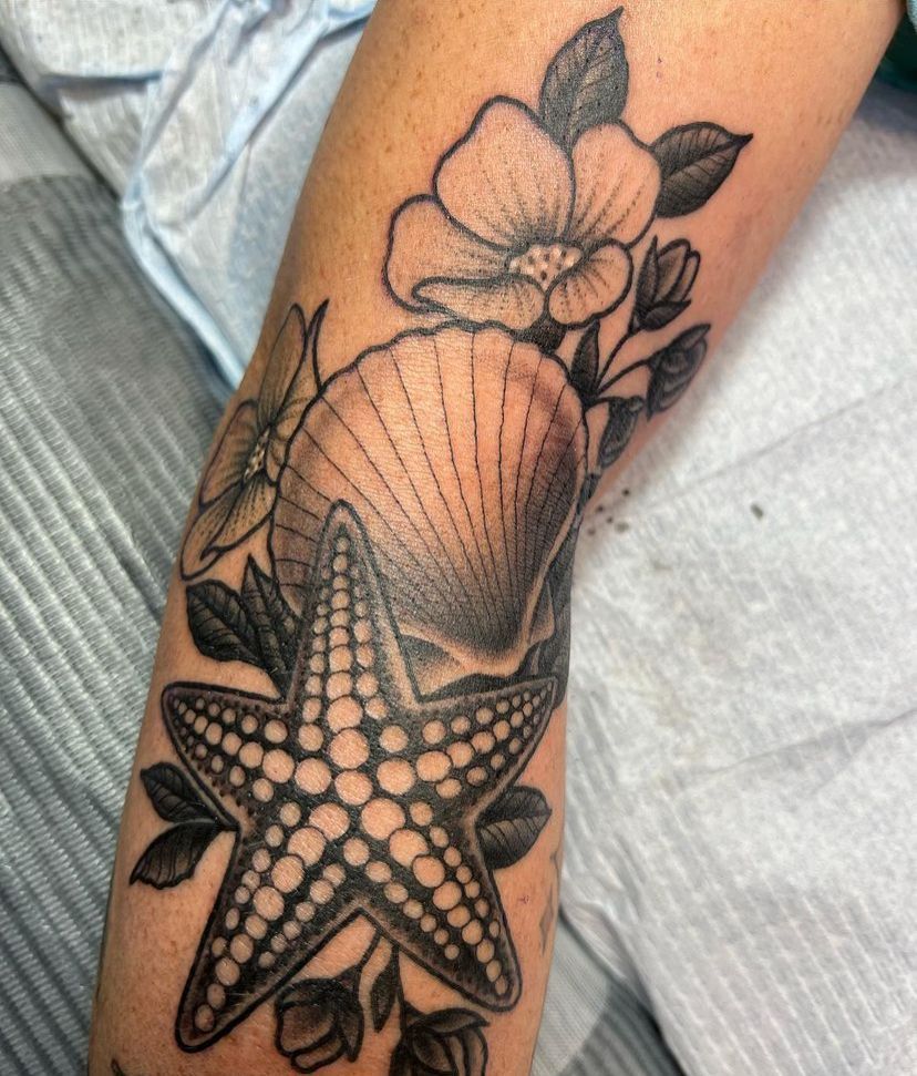 Black-and-gray floral tattoo with a starfish and shell on a forearm