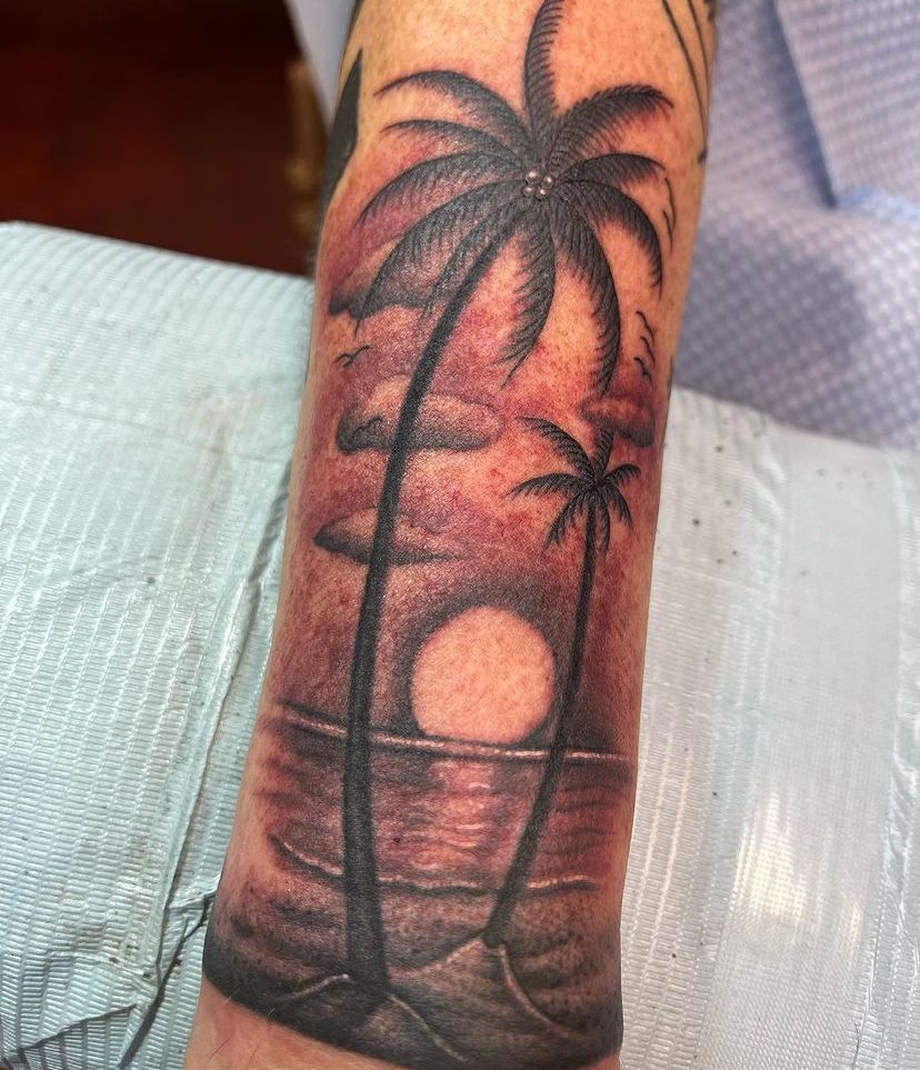 Palm tree sunset tattoo on a forearm with orange sky and ocean reflections