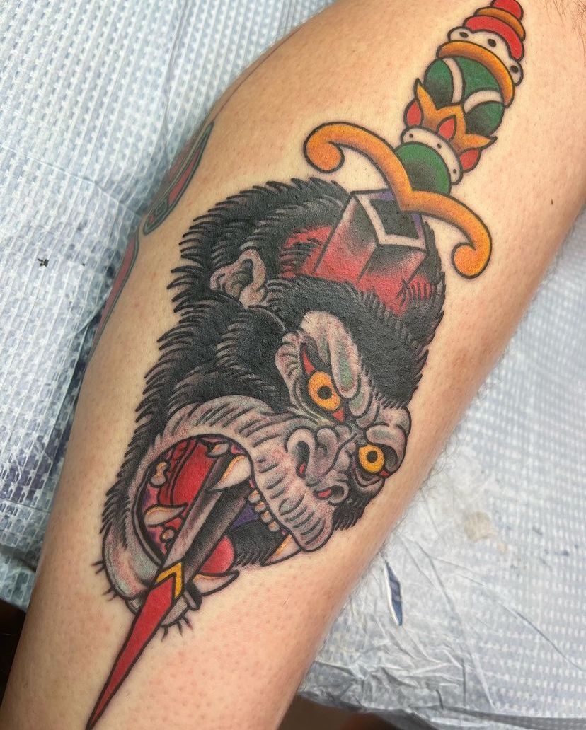 Colorful wolf-head tattoo on an arm, with red eyes and a dagger-like element beneath it.