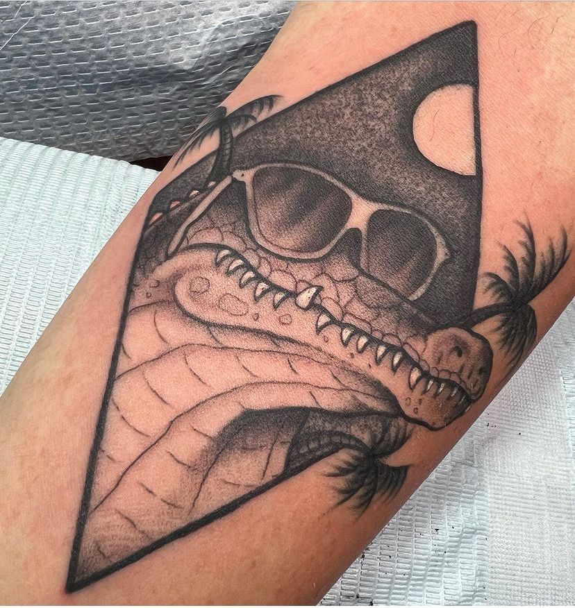 Black-and-gray tattoo of a grinning shark with sunglasses on an arm