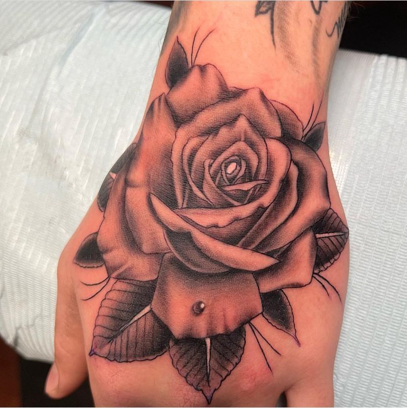 Close-up of a black-and-gray rose tattoo on the back of a hand and wrist