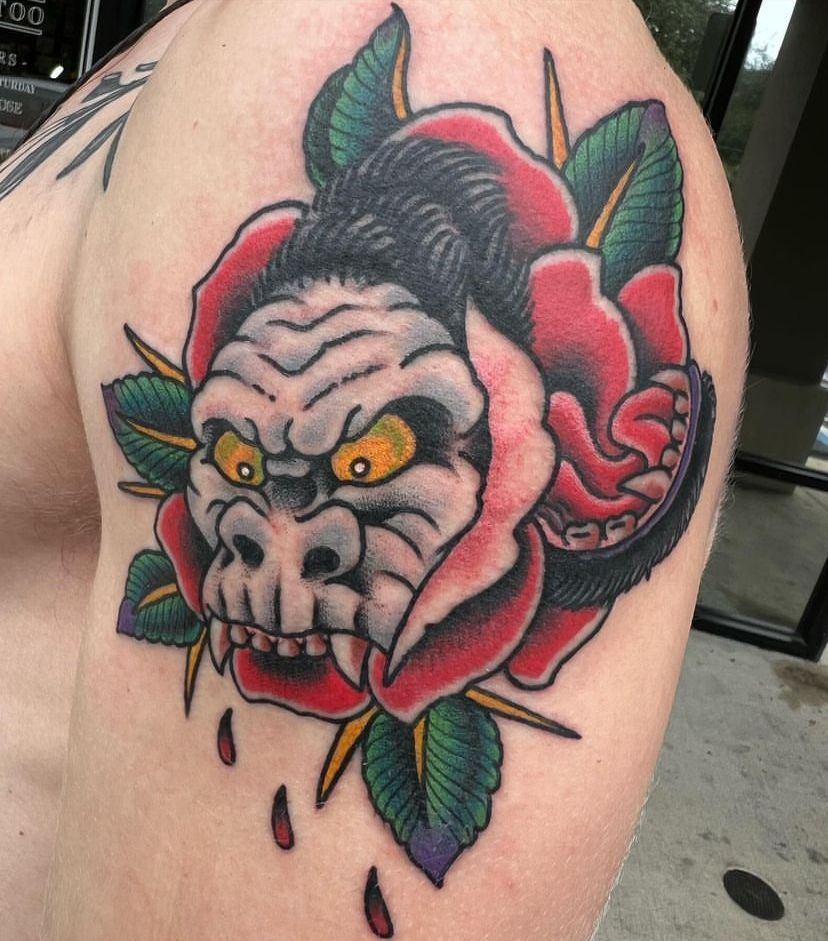 Tattoo of a snarling gray skull with yellow eyes, red rose petals, and green leaves on skin