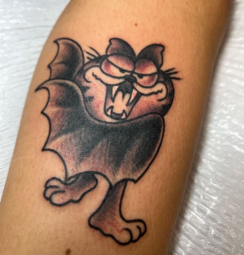 Cartoon bat tattoo with a snarling face, dark wings, and one arm raised on skin