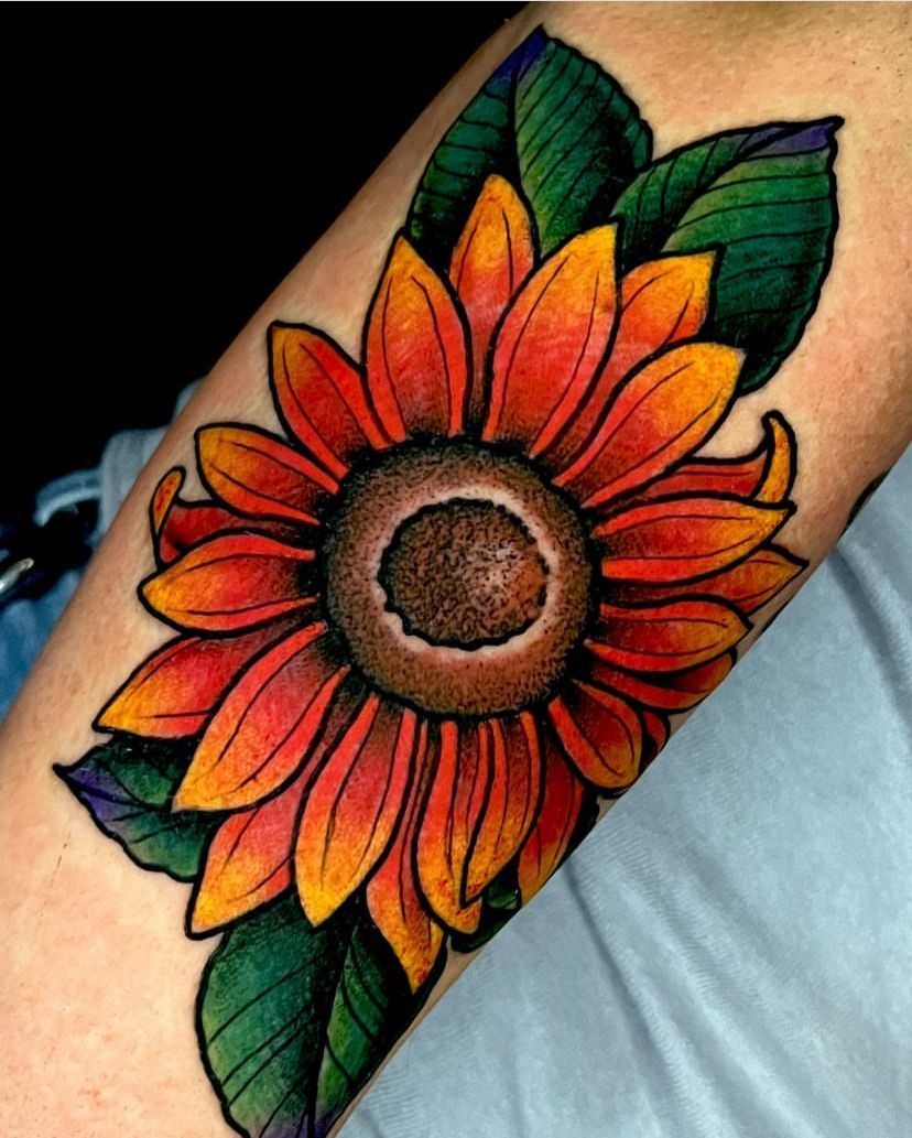 Colorful sunflower tattoo with orange-red petals and green leaves on an arm