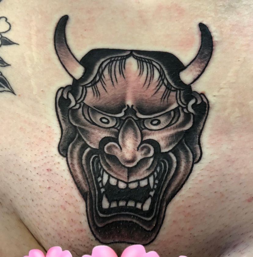 Black horned demon tattoo with an angry face and open mouth on skin.