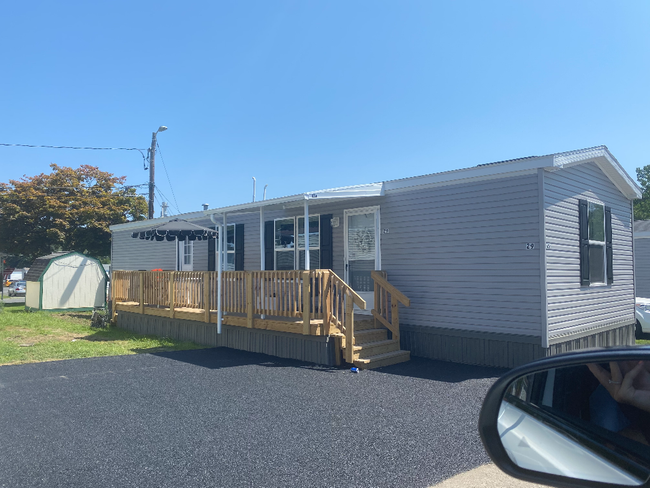 Small gray house with a wooden ramp and porch on a gravel lot, seen from a car window