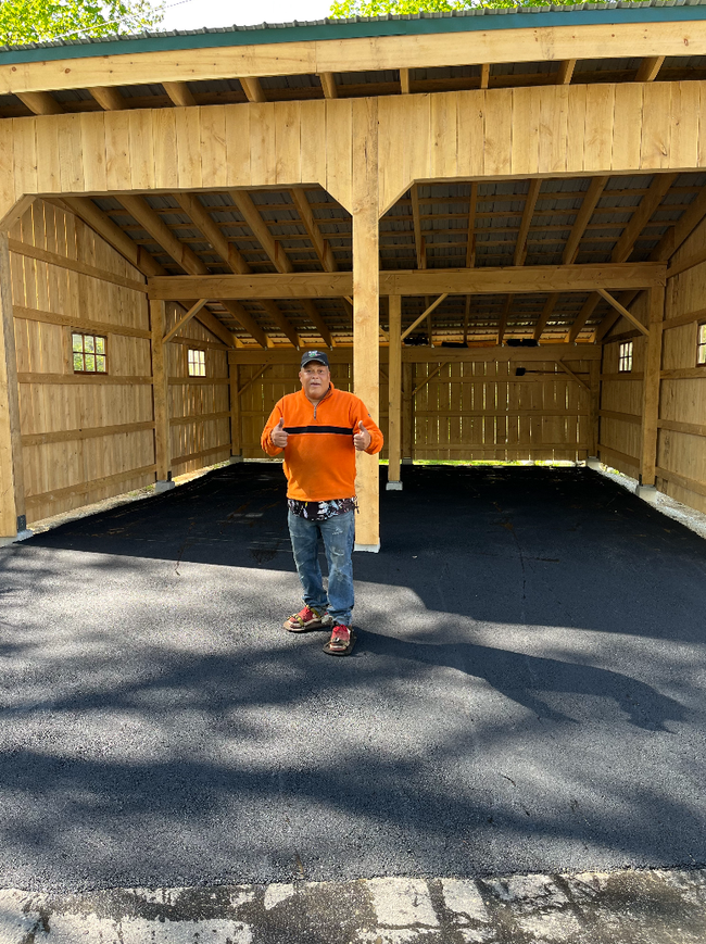 Person standing in front of a wooden shed with a gravel floor and open bays