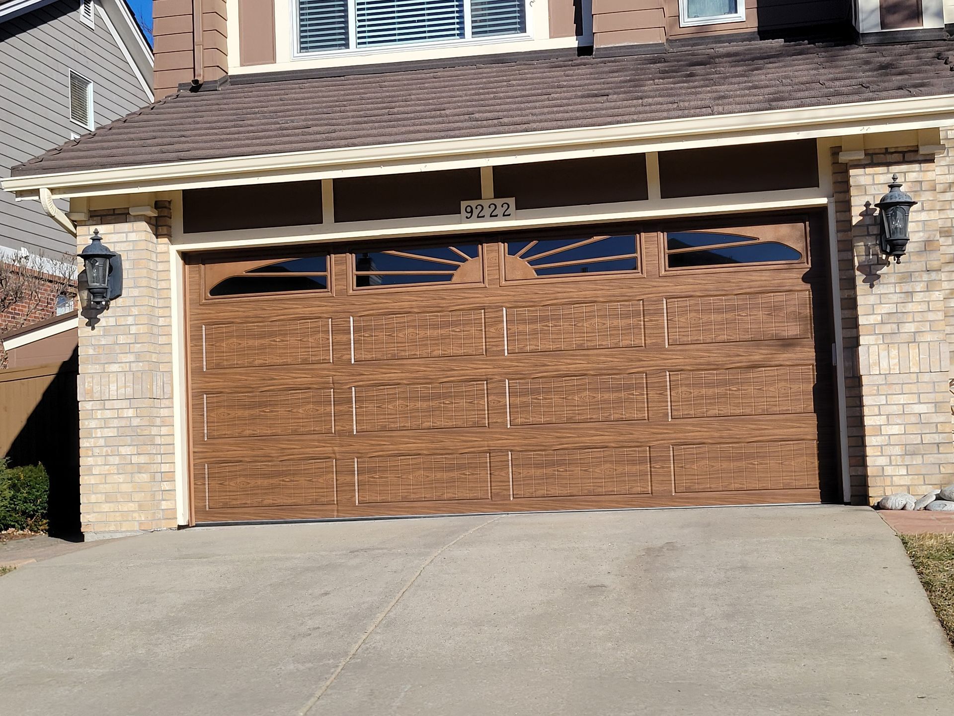 A residential home with a brown, wood-textured garage door featuring sunburst-style window panels.