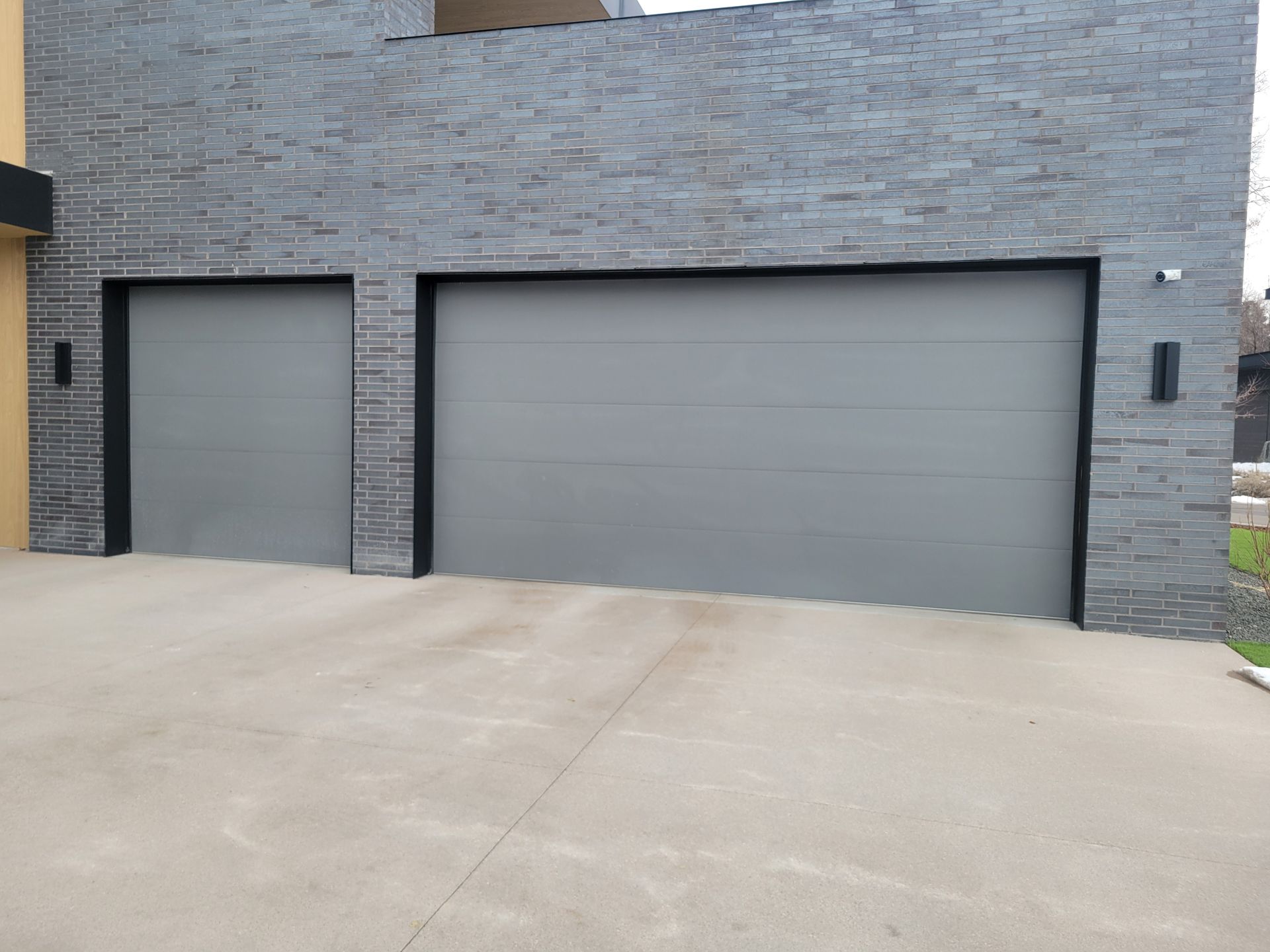 Two gray garage doors set into a dark gray stone-textured wall above a concrete driveway.