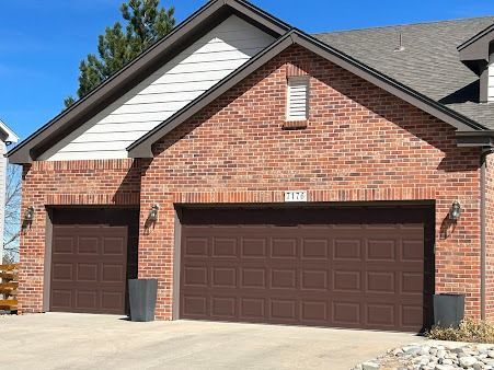 A brick house exterior featuring a two-car garage with dark brown paneled doors under a gabled roof.