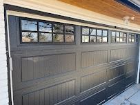 A dark grey garage door with a row of rectangular windows featuring a black grid pattern, installed on a house exterior.