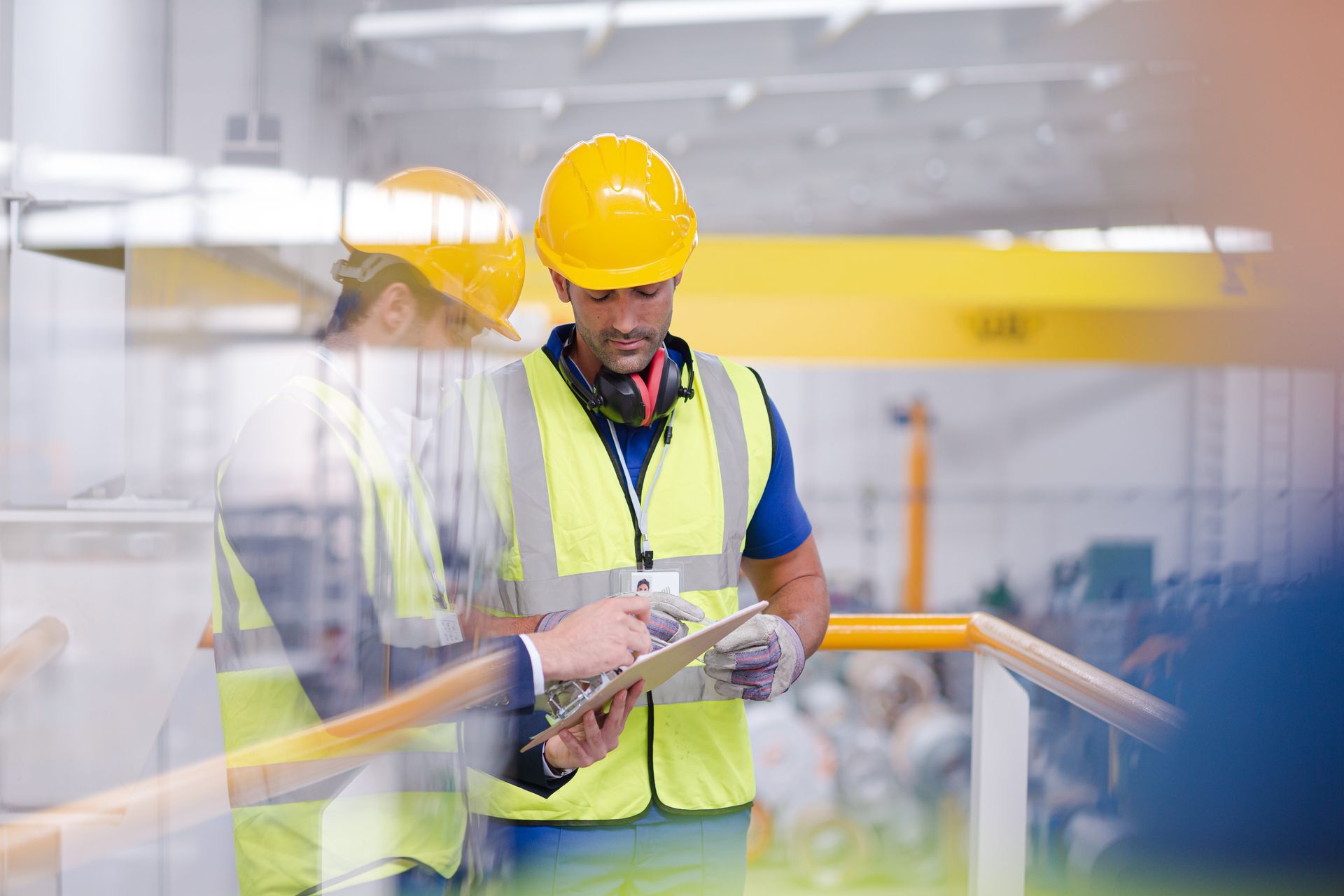 A man in a hard hat is looking at a clipboard in a factory.