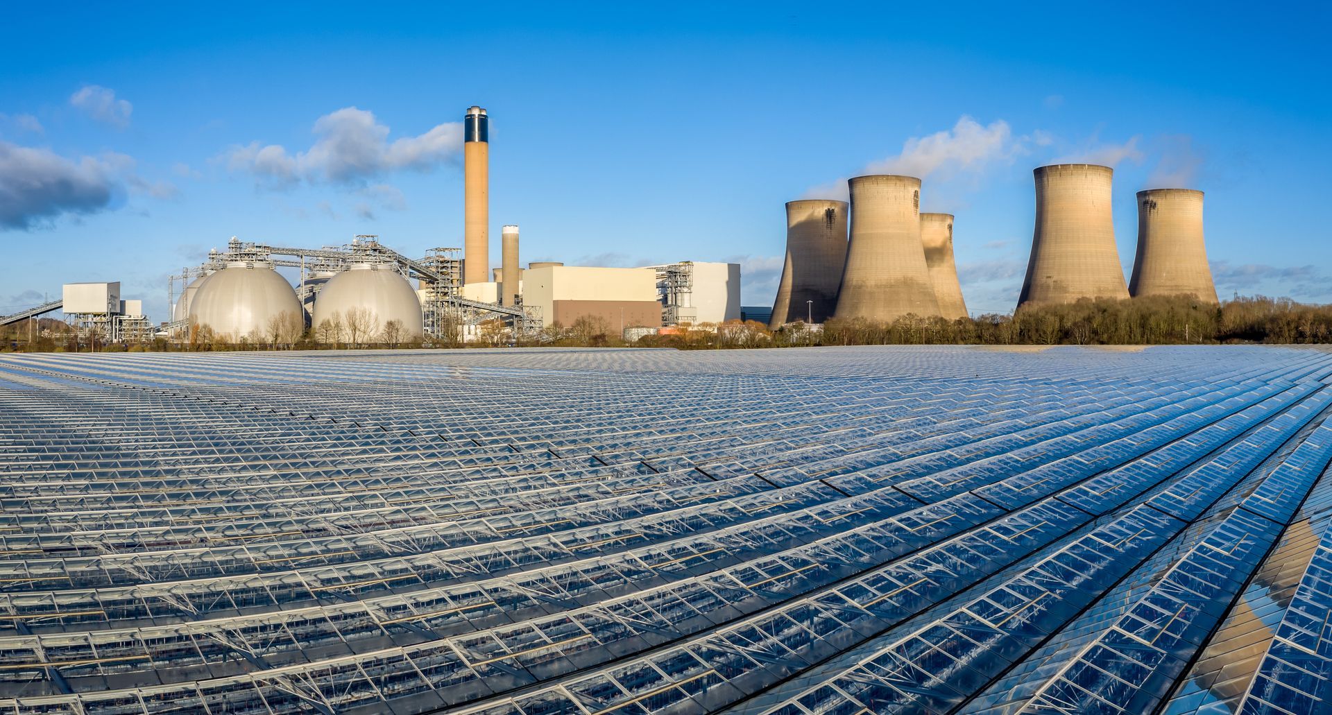 A power plant with a lot of cooling towers and a field of solar panels in front of it.