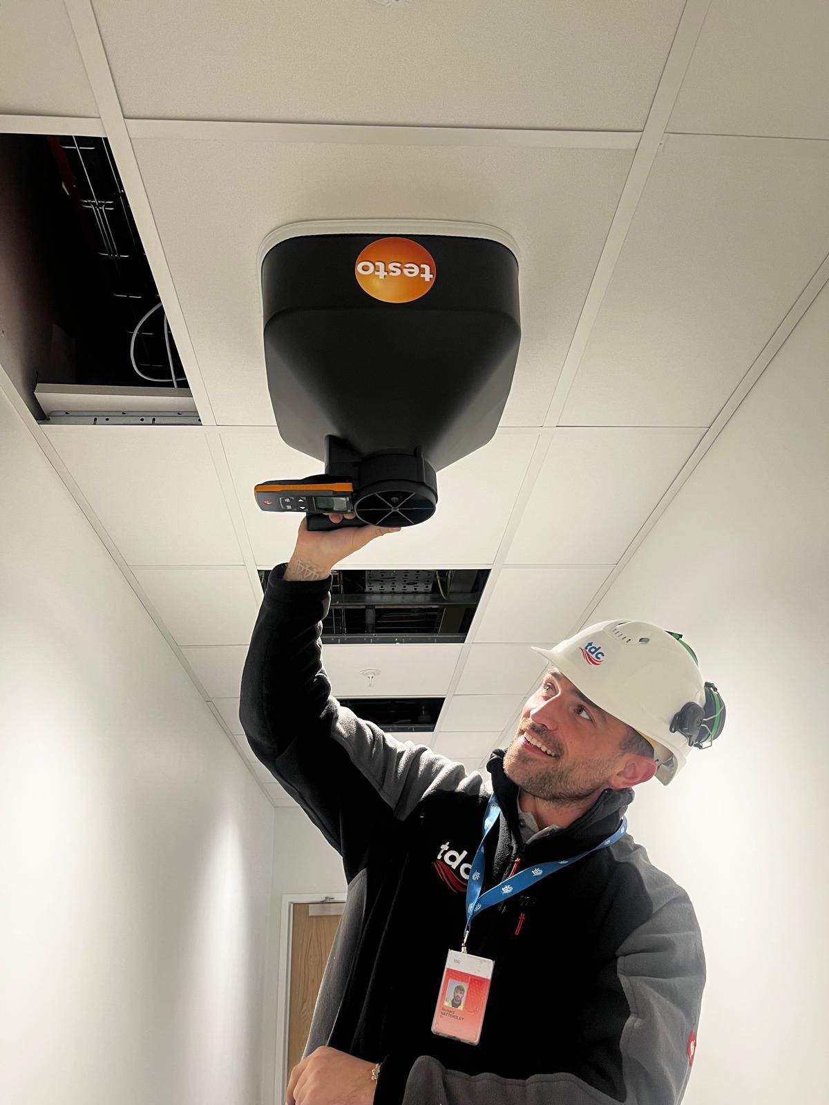 A man in a hard hat is holding a device in a factory.