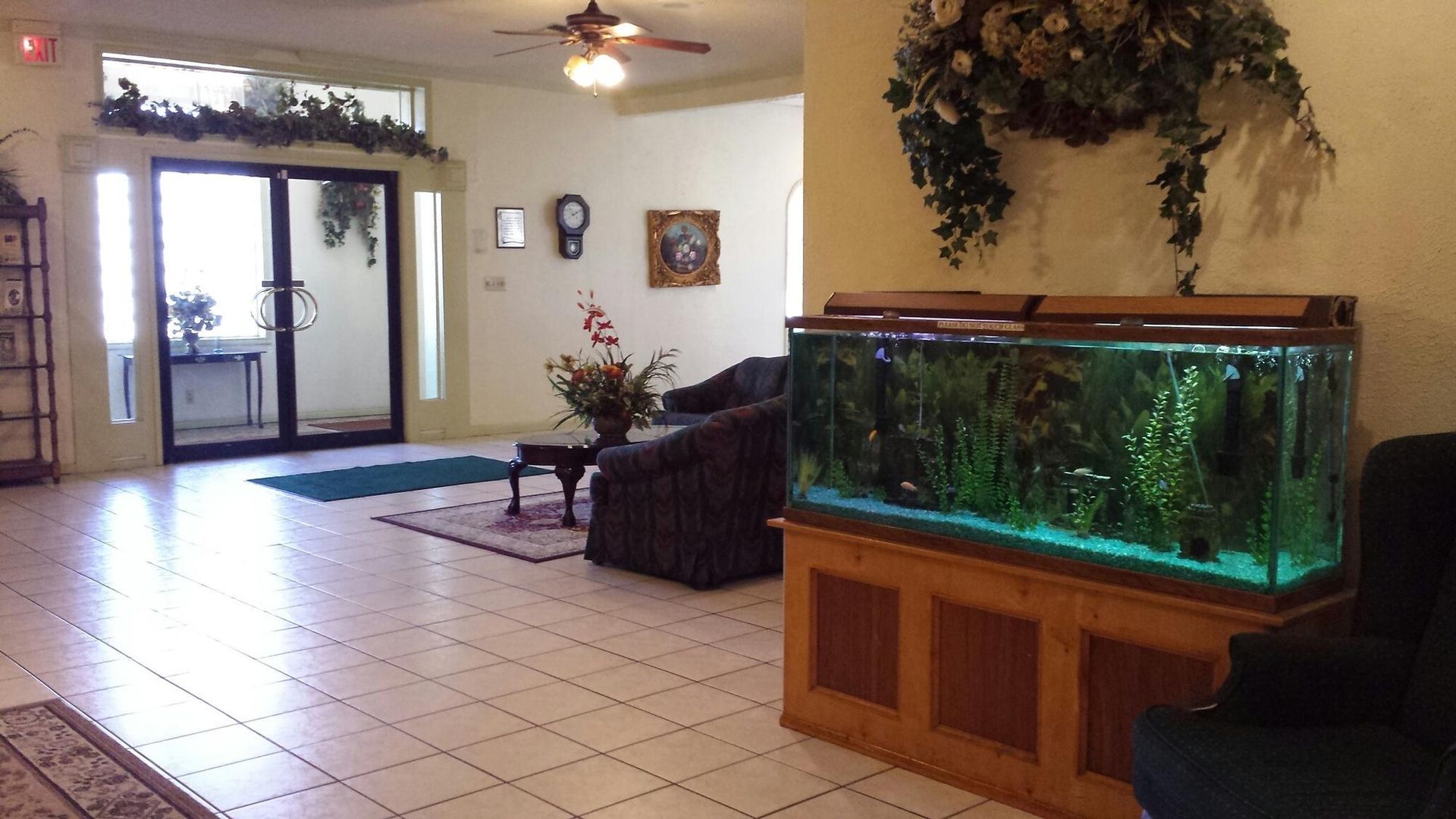 Lobby with large fish tank, seating, and double doors. Artificial plants decorate the ceiling and doorways.