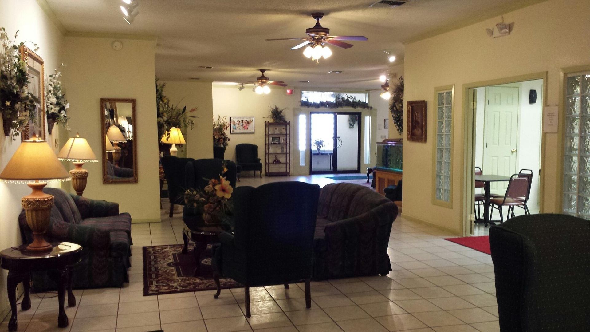 Spacious waiting area with couches, chairs, and potted plants, near an entrance and small dining area.