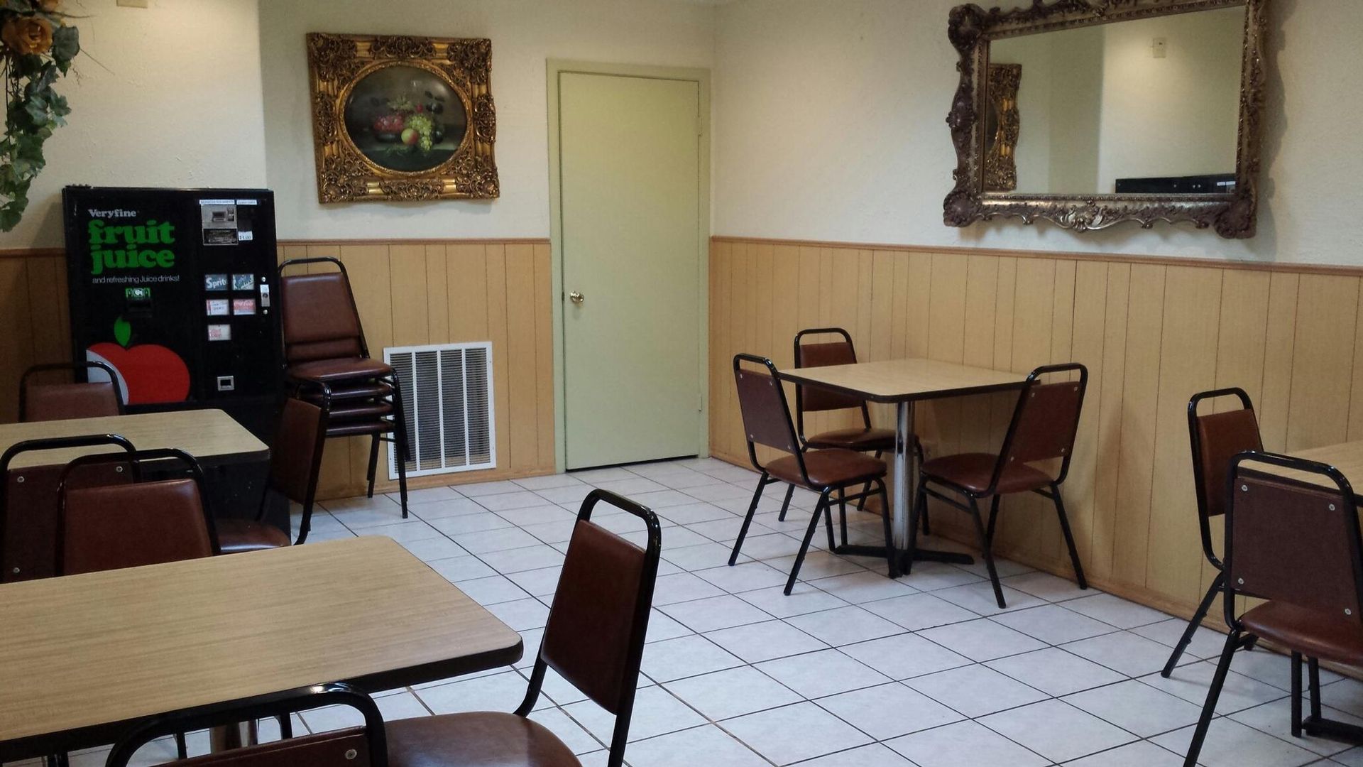 Empty cafe interior with tables, chairs, vending machine, and ornate mirror on the wall.