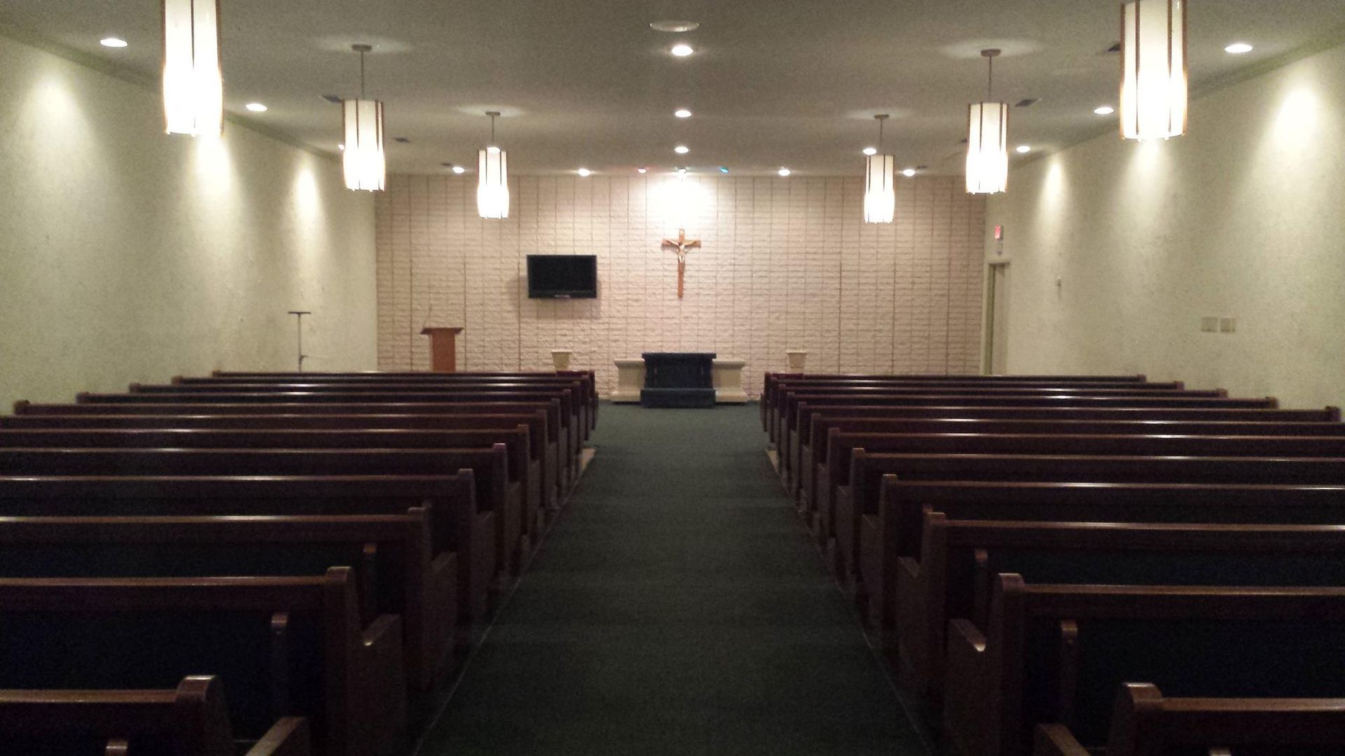 Interior of a funeral home chapel with rows of dark wooden pews facing an altar with a cross.
