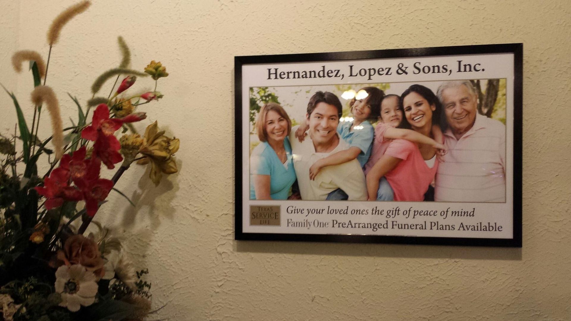 Framed photo: Hernandez, Lopez & Sons, Inc. family portrait, floral arrangement to the left.