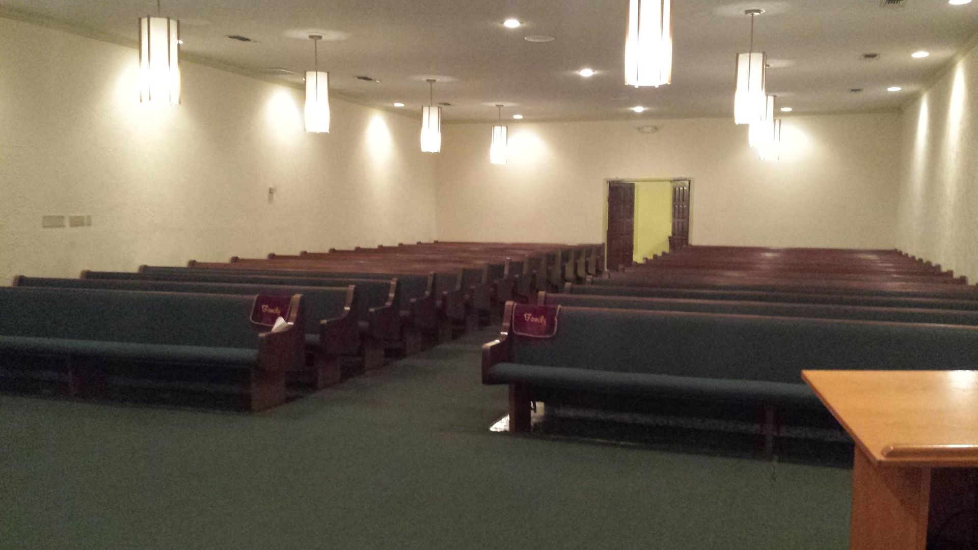 Interior of a chapel with rows of green pews and hanging lights.
