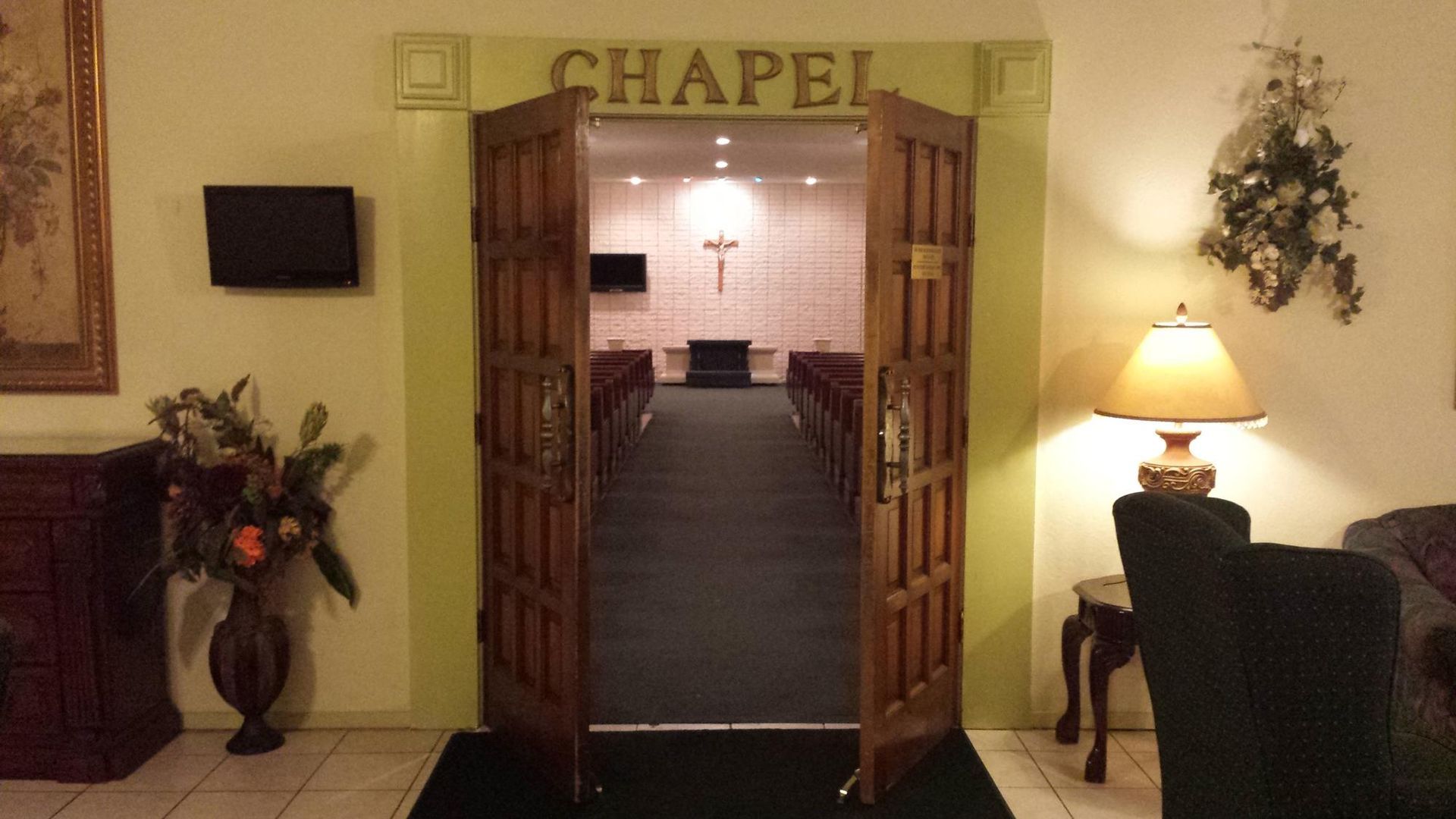 Open double wooden doors lead into a chapel. Interior has pews, cross, and a small altar.