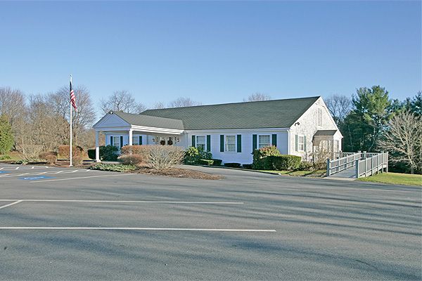 Small white church building with green roof beside a parking lot on a sunny day