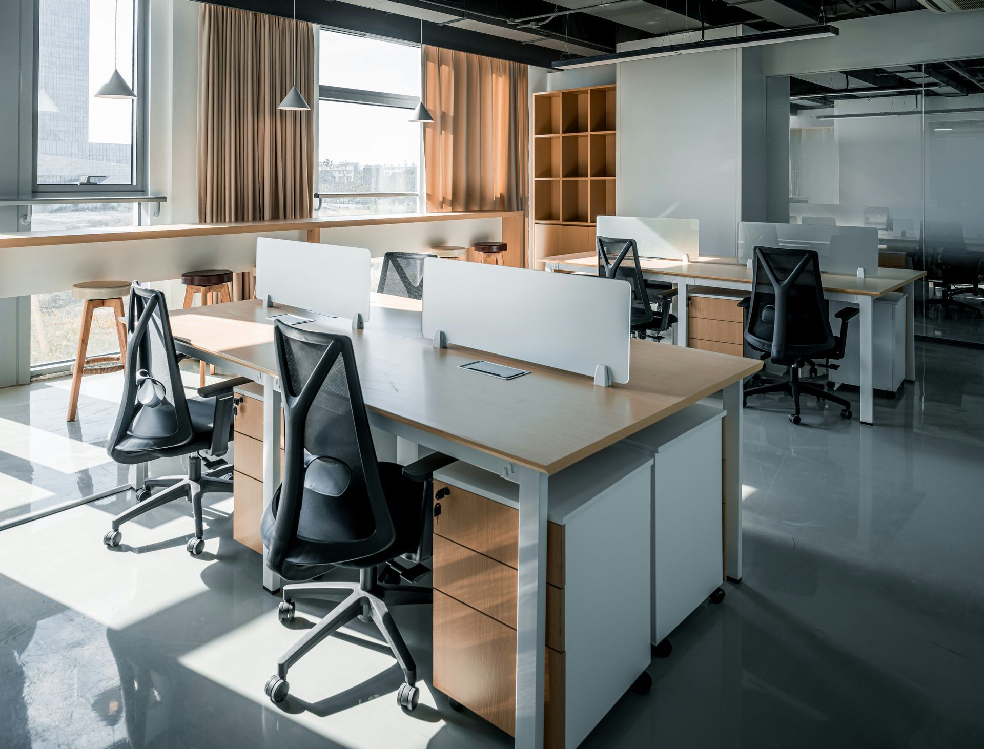 Office space with desks, chairs, and natural light from large windows.